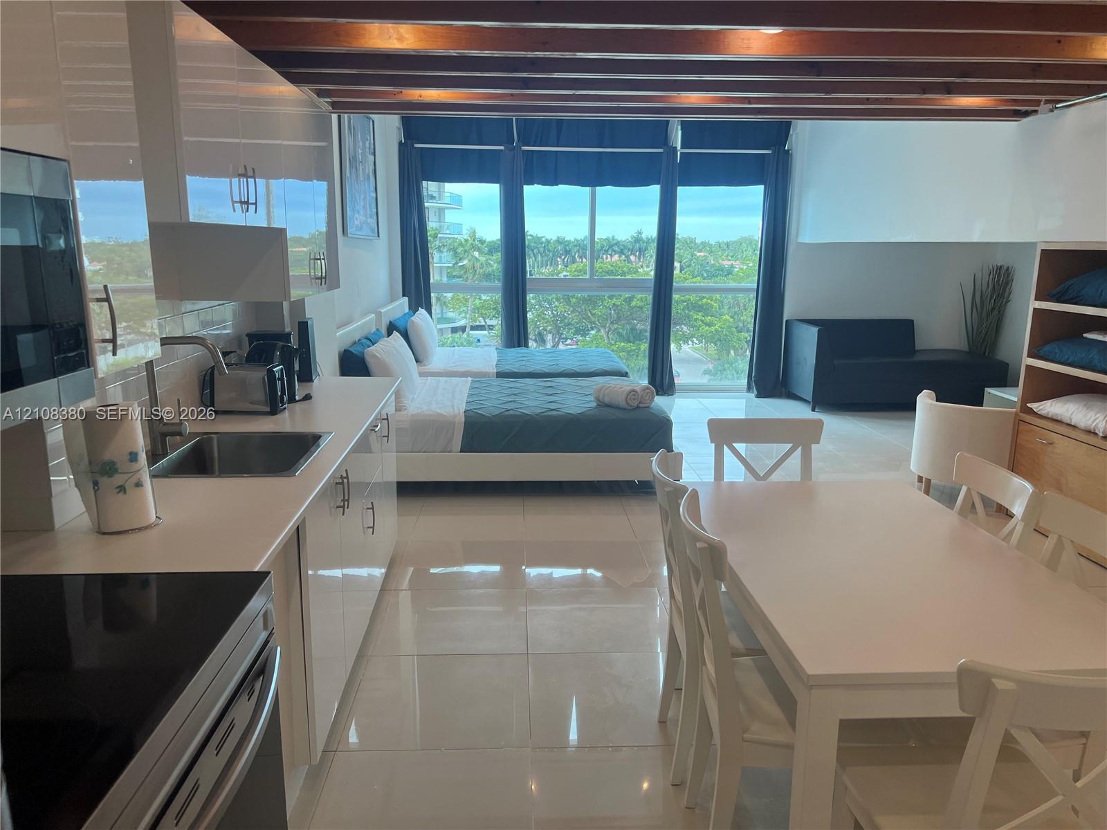 High-gloss cabinetry, stainless steel sink, tile flooring, exposed wood ceiling beams, and floor-to-ceiling windows High-gloss cabinetry, stainless steel sink, tile flooring, exposed wood ceiling beams, and floor-to-ceiling windows