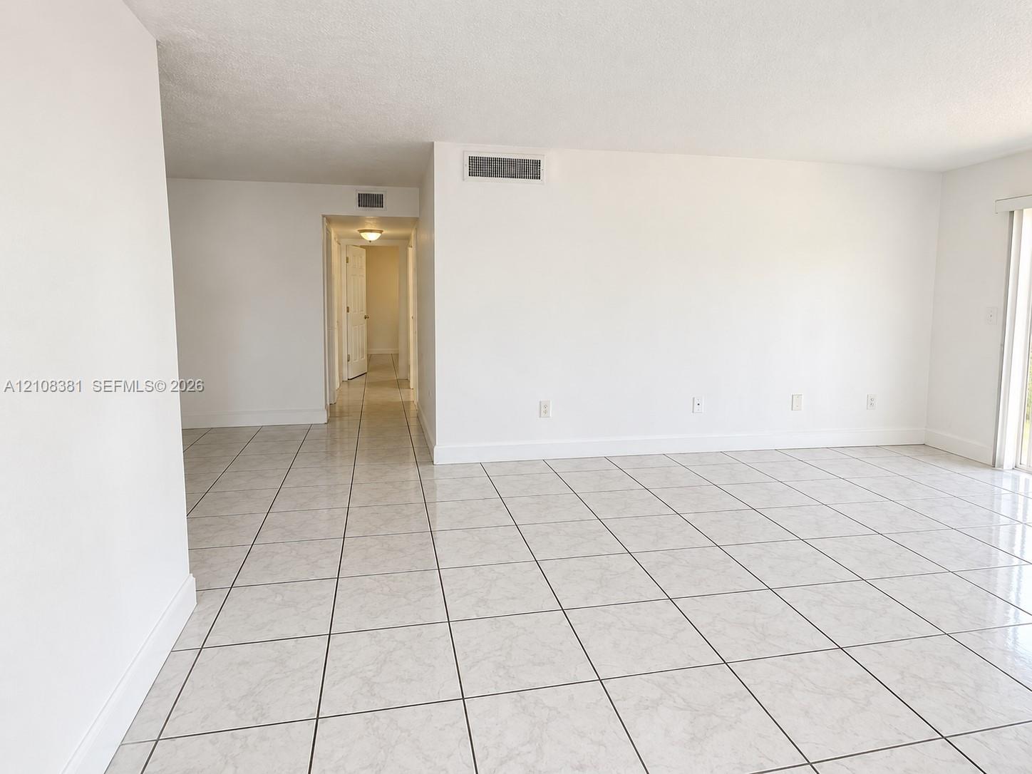 Neutral-toned interior space featuring glossy, square-format ceramic tile flooring, expansive smooth-finish white walls, and a large, multi-pane window with integrated blinds
