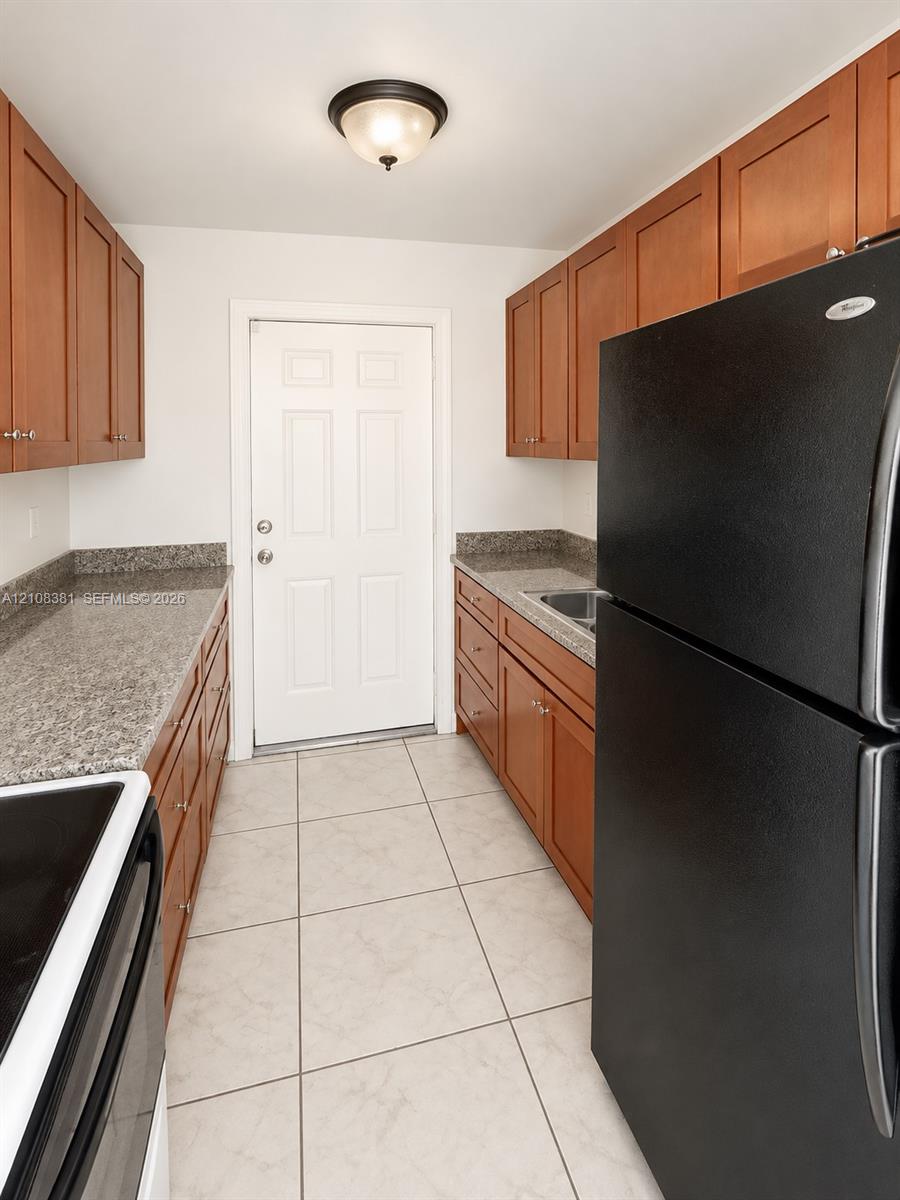 Kitchen featuring wood cabinetry, stone-finish countertops, tile flooring, and a flush-mount ceiling fixture