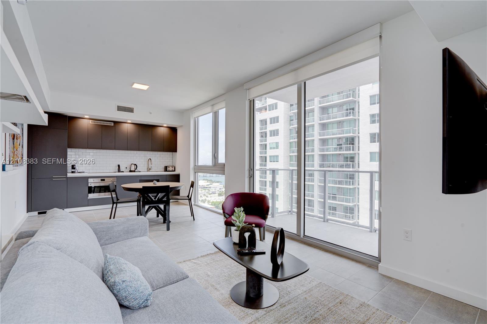Modern kitchen featuring dark cabinetry, white subway tile backsplash, and stainless-steel built-in appliances, complemented by floor-to-ceiling windows and large-format tile flooring
