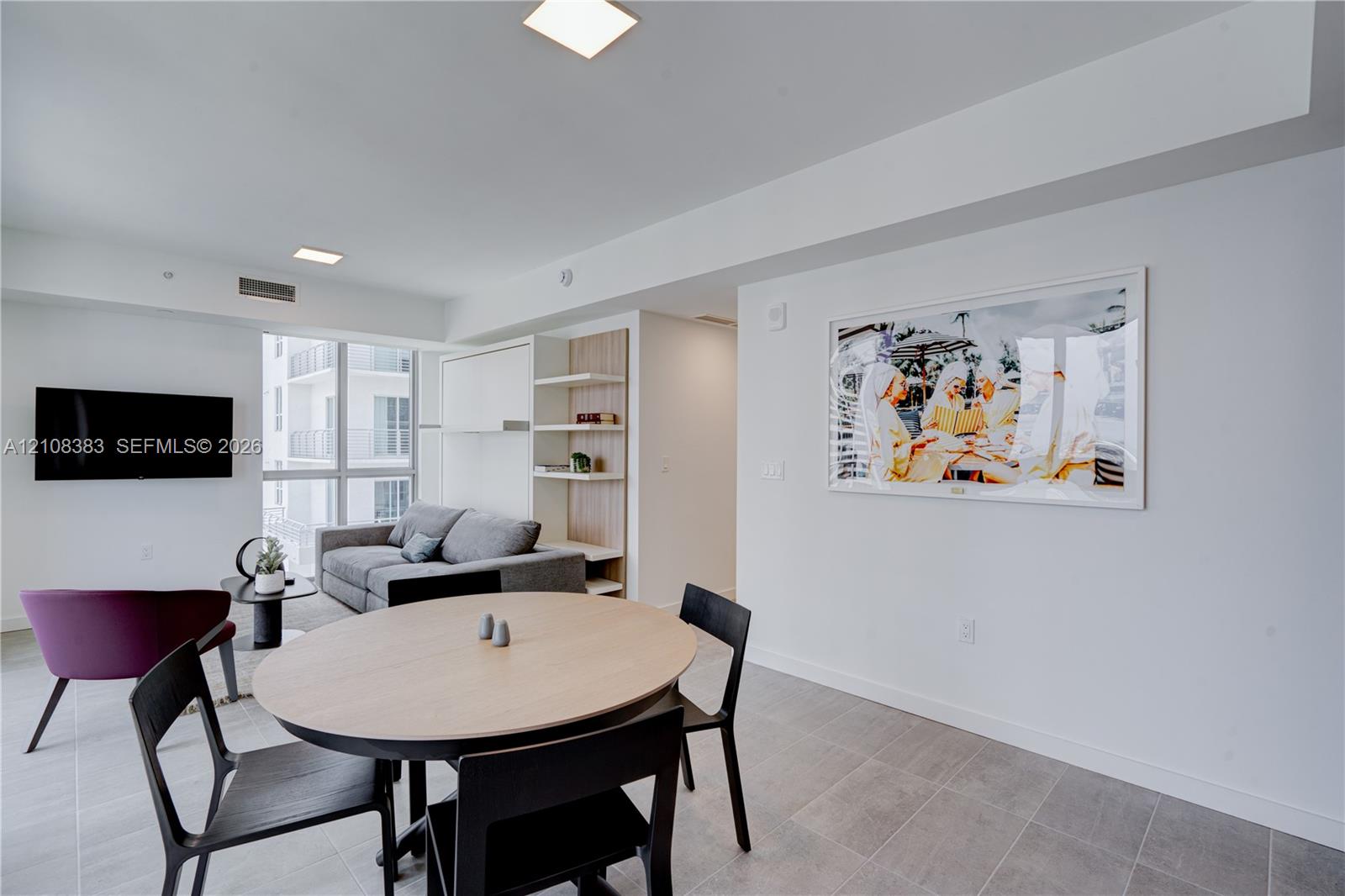 Open-concept area featuring tile flooring, floor-to-ceiling windows, recessed square lighting, and built-in wood-tone shelving Open-concept area featuring tile flooring, floor-to-ceiling windows, recessed square lighting, and built-in wood-tone shelving