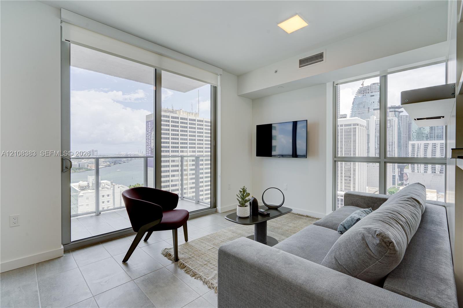 Floor-to-ceiling windows, ceramic tile flooring, sliding glass door, private balcony, and urban cityscape backdrop Floor-to-ceiling windows, ceramic tile flooring, sliding glass door, private balcony, and urban cityscape backdrop