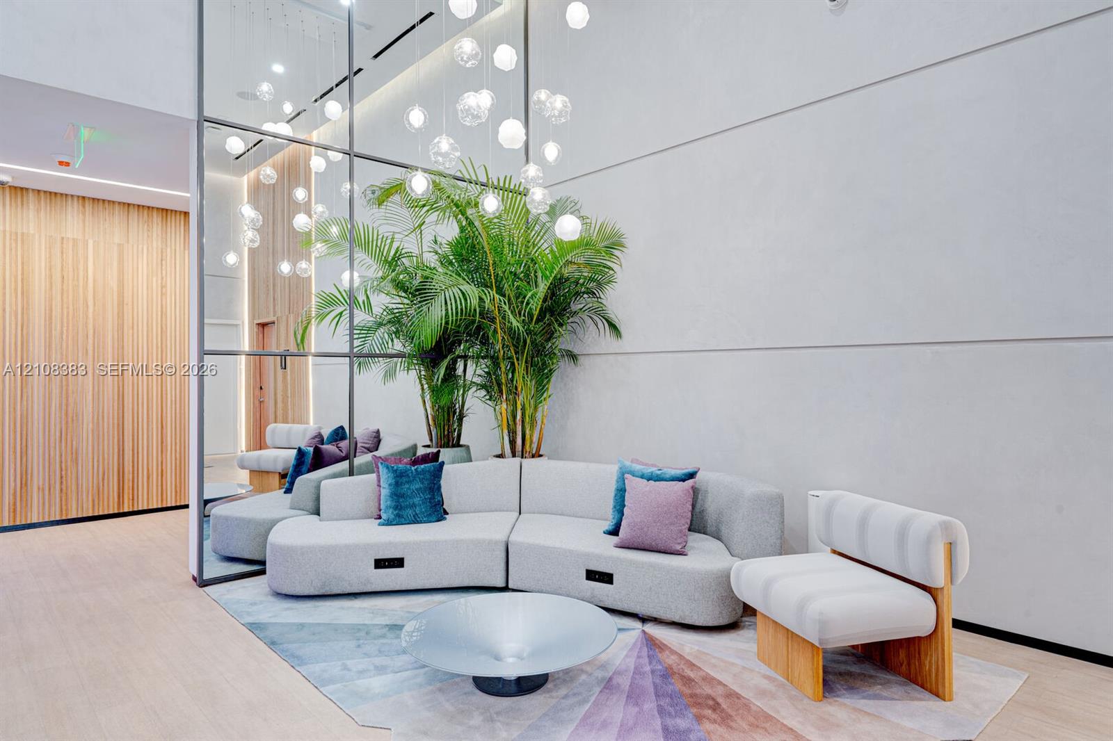 Double-height ceilings featuring a floor-to-ceiling grid mirror wall, recessed linear lighting, vertical wood-slat accent paneling, and a multi-tiered glass sphere chandelier