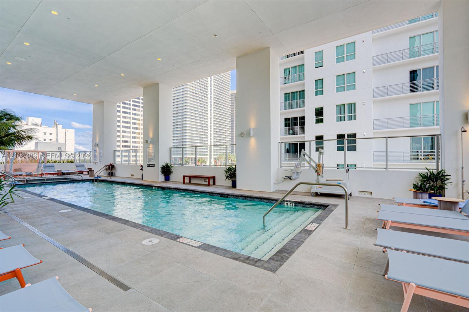Covered swimming pool featuring built-in entry steps, stainless steel handrails, expansive stone-tile decking, and recessed lighting