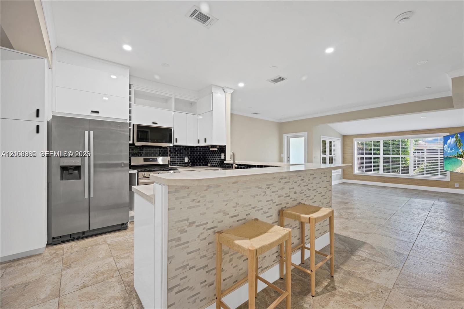 Kitchen featuring white flat-panel cabinetry, stainless steel appliances, a stone-tile breakfast bar, and tile flooring Kitchen featuring white flat-panel cabinetry, stainless steel appliances, a stone-tile breakfast bar, and tile flooring