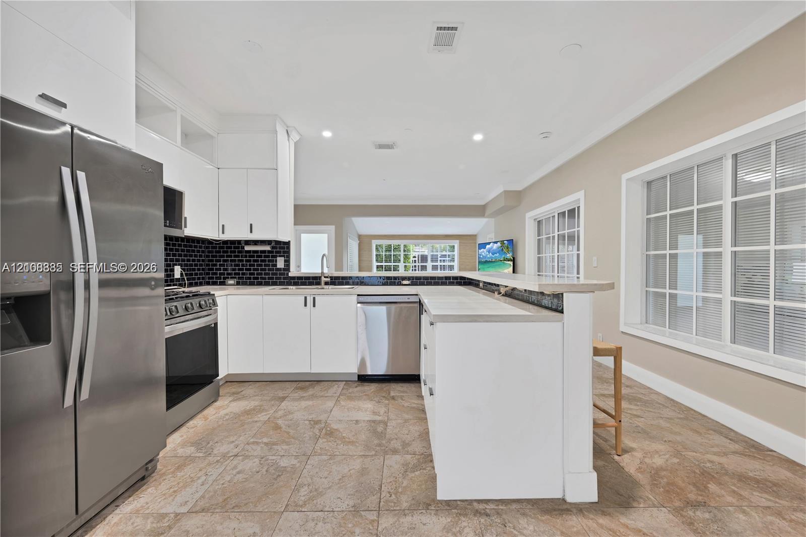 Kitchen featuring white shaker cabinetry, stainless steel appliances, a black tiled backsplash, a stone-finish countertop peninsula, and ceramic tile flooring Kitchen featuring white shaker cabinetry, stainless steel appliances, a black tiled backsplash, a stone-finish countertop peninsula, and ceramic tile flooring