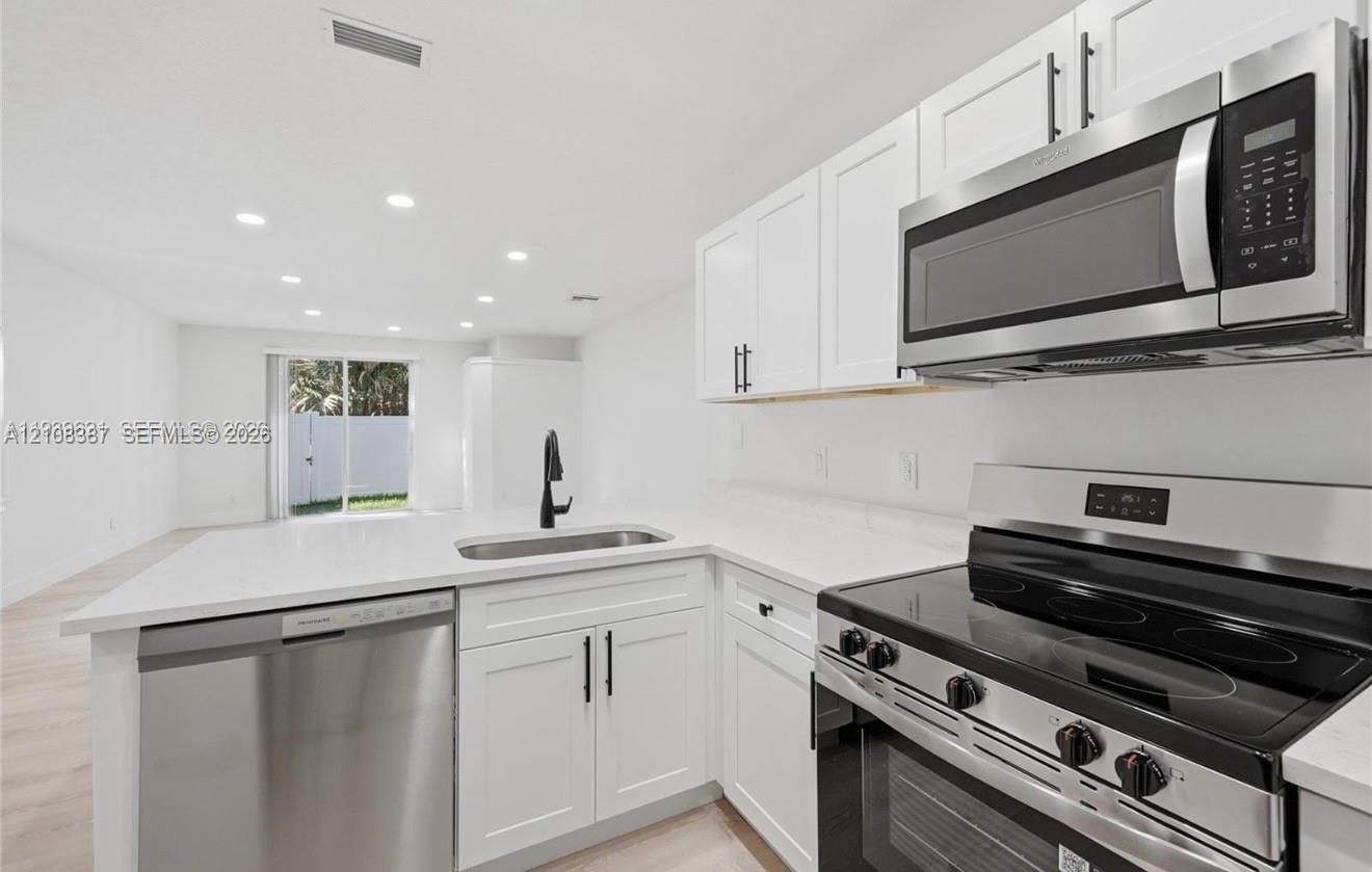 Kitchen featuring white shaker-style cabinetry, quartz countertops, stainless steel appliances, and a matte black gooseneck faucet