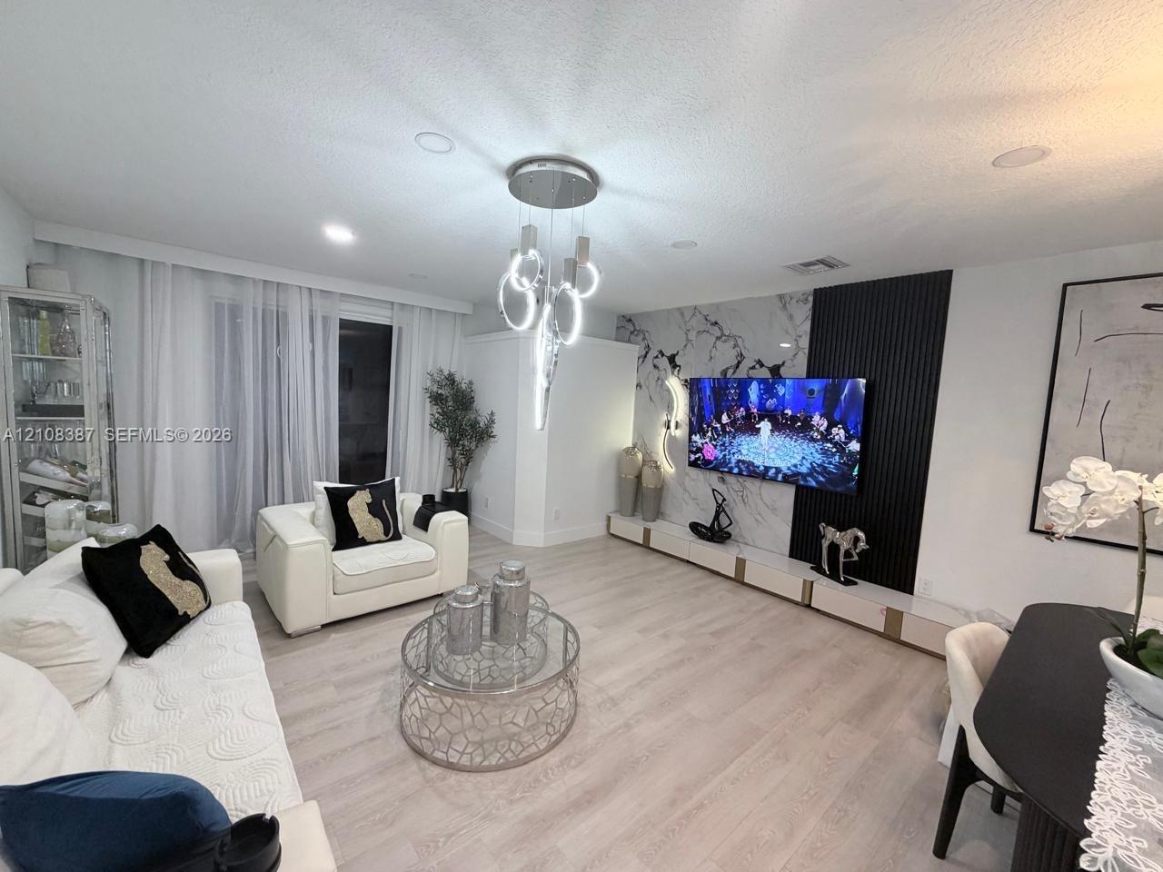 Living area featuring wood-finish flooring, recessed lighting, a modern multi-pendant chandelier, and a custom accent wall with integrated stone-patterned surfacing and vertical slat detailing