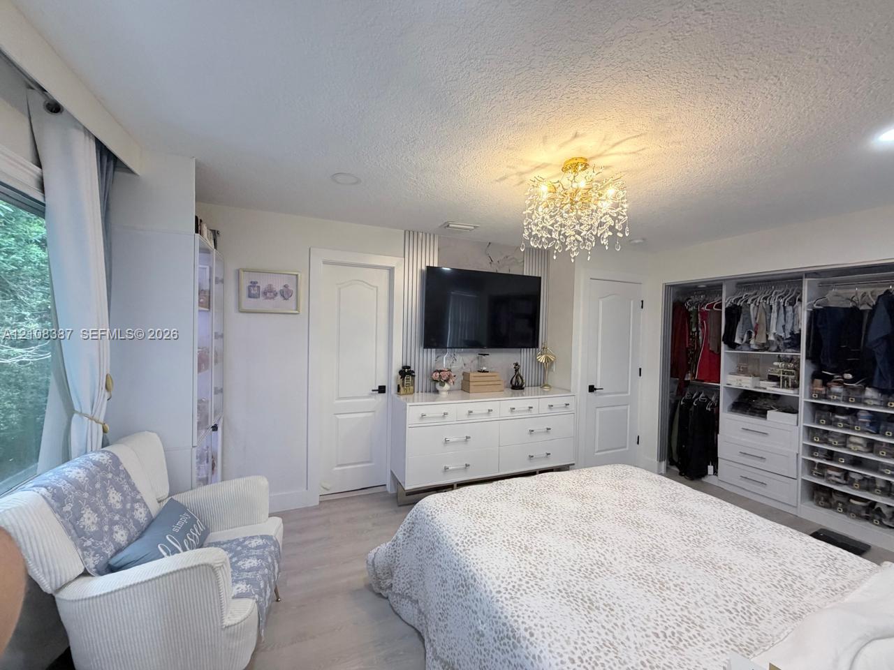 Light-toned wood-finish flooring, custom built-in wardrobe cabinetry with integrated drawer organization, crystal-style chandelier lighting, vertical wall paneling, and interior paneled doors