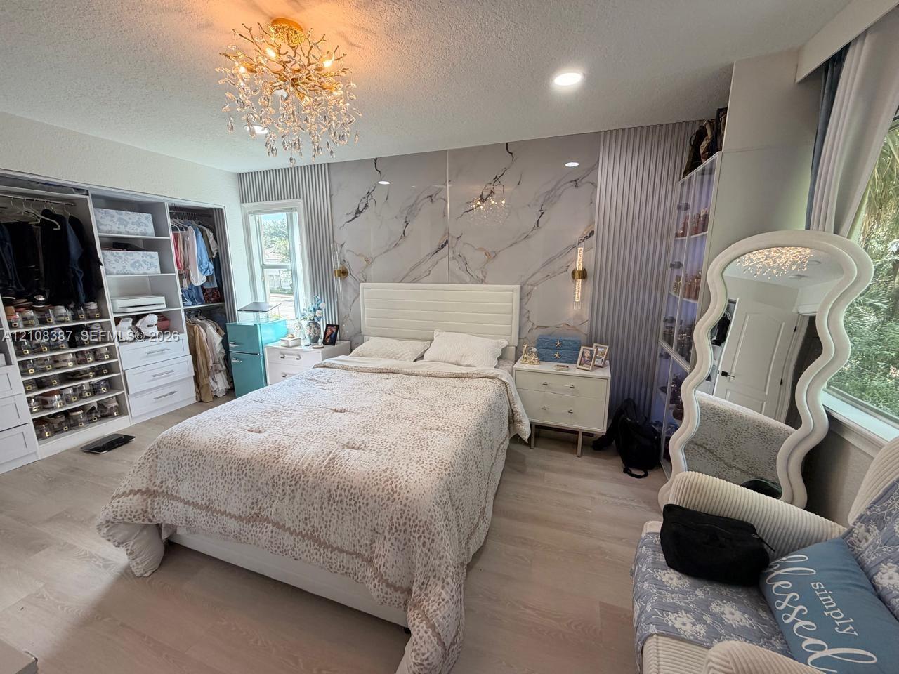 Bedroom featuring wood-finish flooring, custom built-in wardrobe shelving, a stone-pattern accent wall, and a multi-tiered crystal chandelier