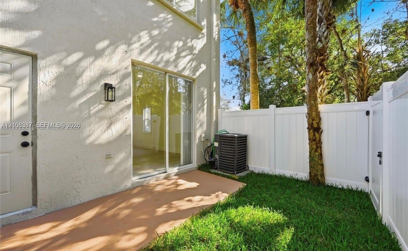 Stucco exterior featuring a concrete patio, sliding glass door, and a private fenced-in yard with mature palms