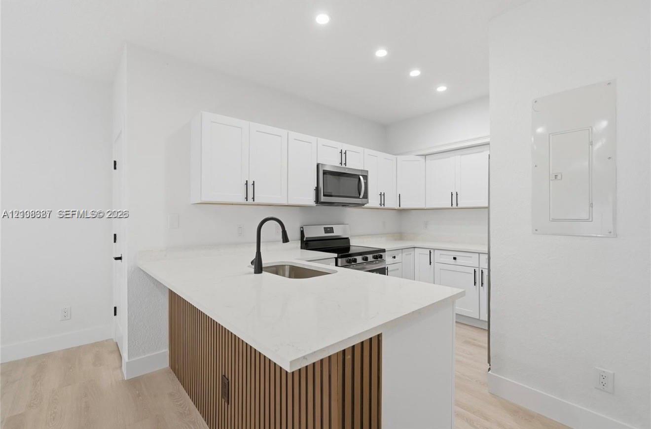 Kitchen featuring white shaker-style cabinetry, quartz countertops, a slatted wood-finish island base, a matte black arched faucet, and recessed ceiling lighting