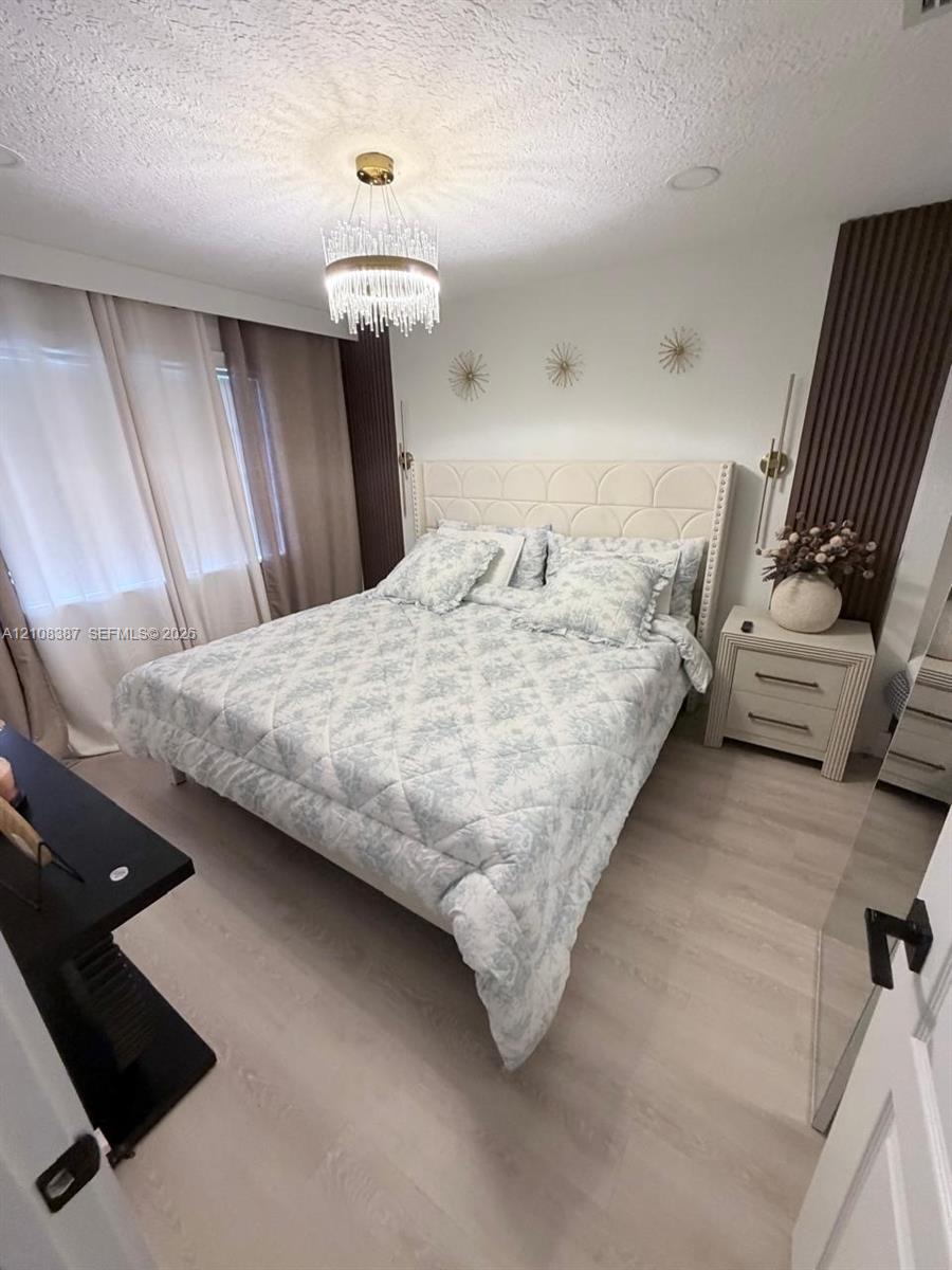 Bedroom featuring light wood-finish flooring, vertical slat wall paneling, and a tiered crystal chandelier