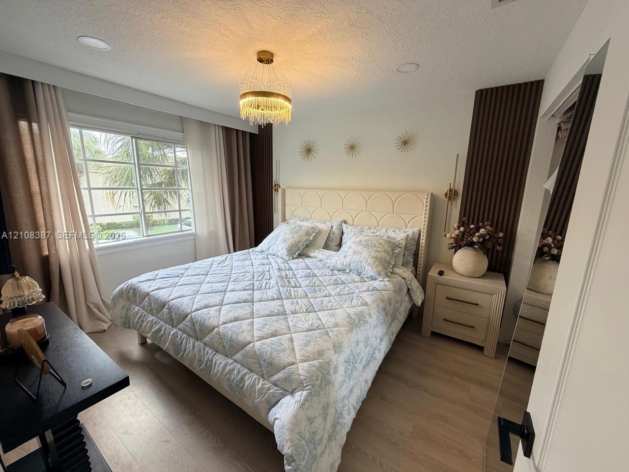 Bedroom featuring recessed ceiling lighting, a circular tiered crystal chandelier, wood-finish flooring, and vertical wood-slat accent wall detailing