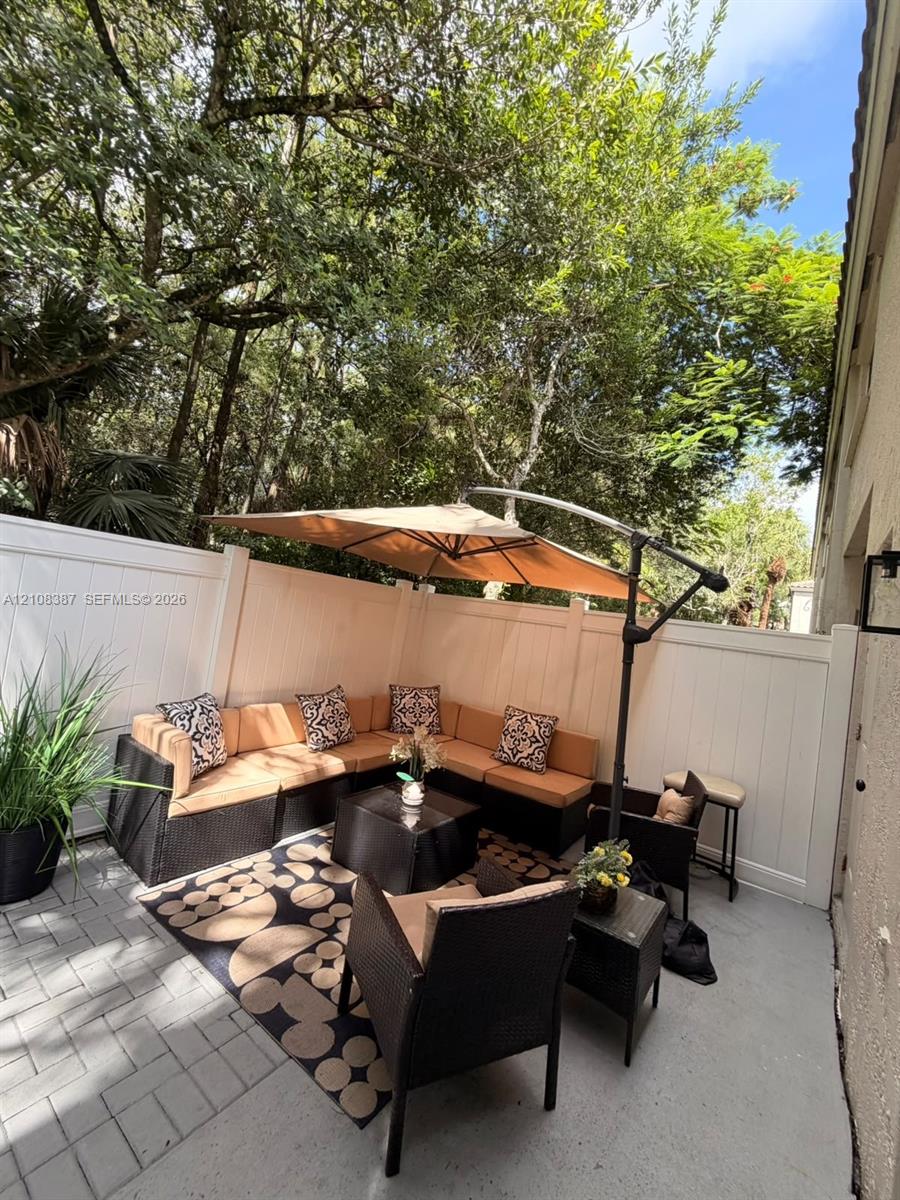 Private outdoor patio featuring light-toned concrete hardscaping and a solid white vinyl privacy fence set against mature trees