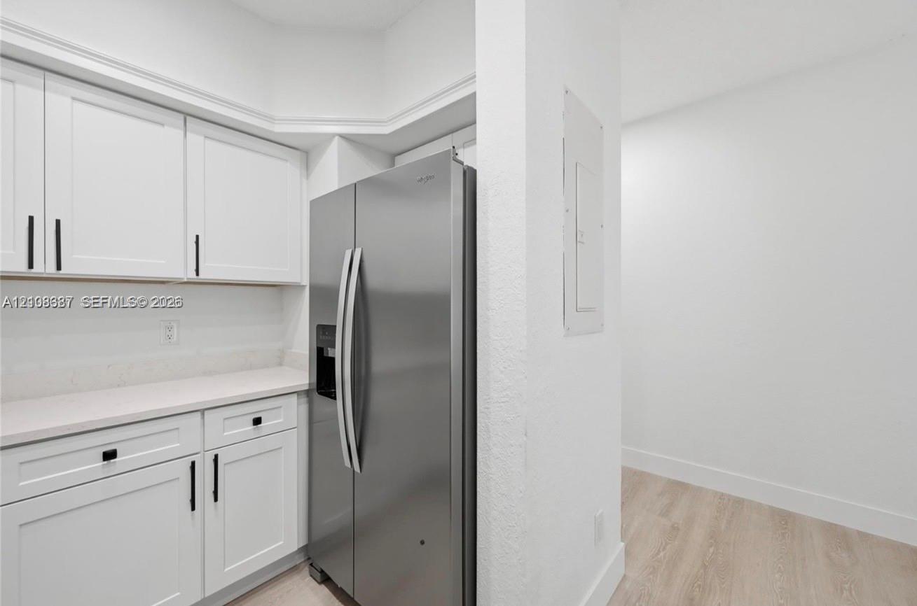 White shaker-style cabinetry with matte black hardware, stone-finish countertops, and a side-by-side stainless steel refrigerator with light-tone wood-finish flooring
