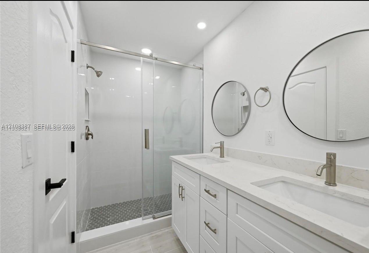 Dual vanity with white cabinetry, stone-surface countertop, and dual round mirrors