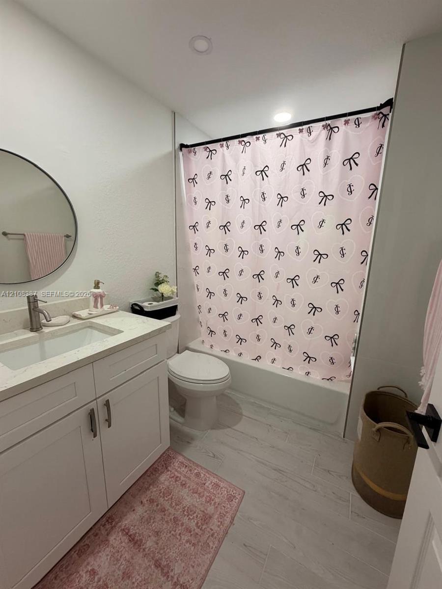 White shaker-style vanity with a solid surface countertop, integrated sink, circular wall-mounted mirror, and tile flooring