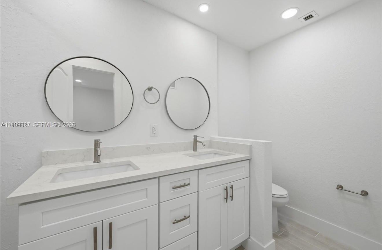 Dual-sink vanity featuring white cabinetry, stone-finish countertops, circular wall-mounted mirrors, and chrome-finish faucets