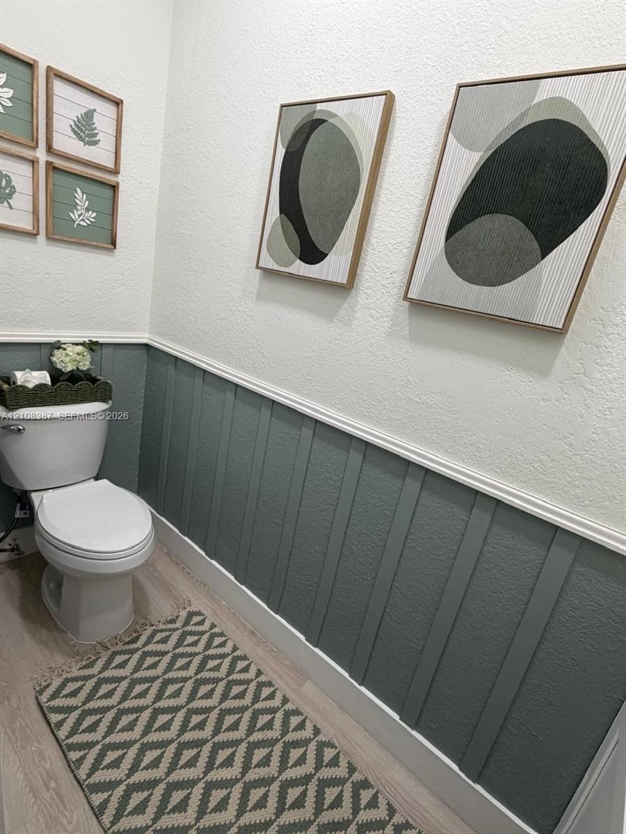 Powder room featuring board and batten wainscoting, wood-finish flooring, and a porcelain toilet