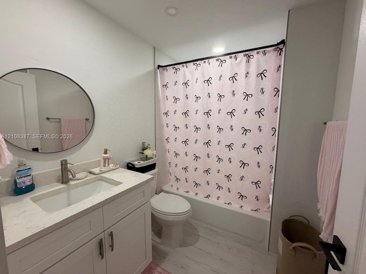 Bathroom featuring a vanity with a light-toned stone countertop, integrated sink, circular mirror, and wood-finish flooring