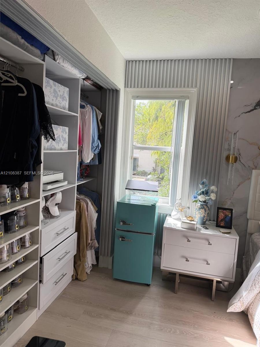 Custom walk-in closet featuring white built-in shelving and drawers, vertical slat wall paneling, stone-patterned accent wall, and wood-finish flooring