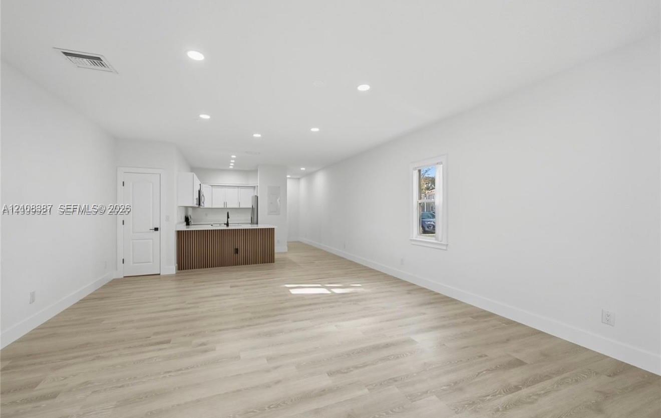 Open interior featuring wood-finish flooring, recessed lighting, and a kitchen peninsula with fluted detailing