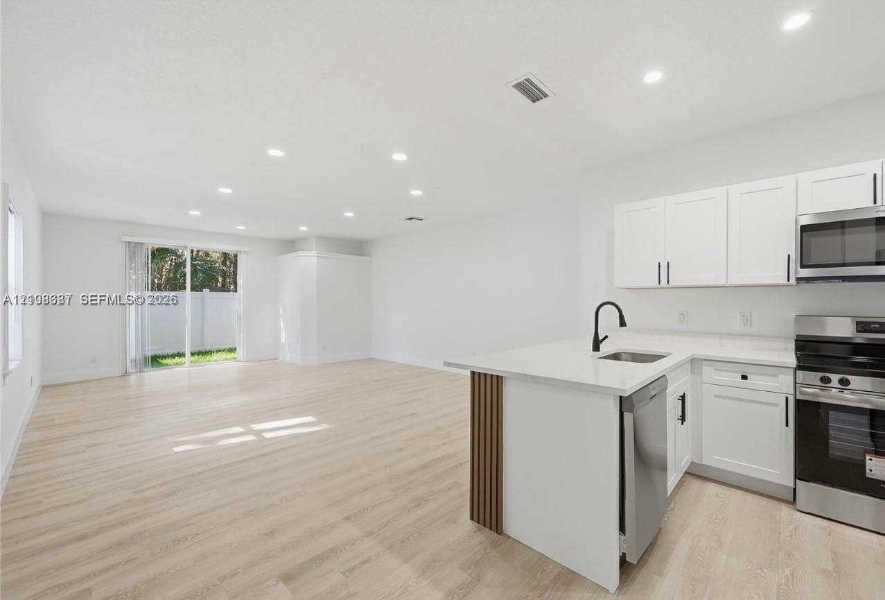 Open-concept kitchen featuring white shaker-style cabinetry, quartz countertops, a matte black faucet, and wood-finish flooring