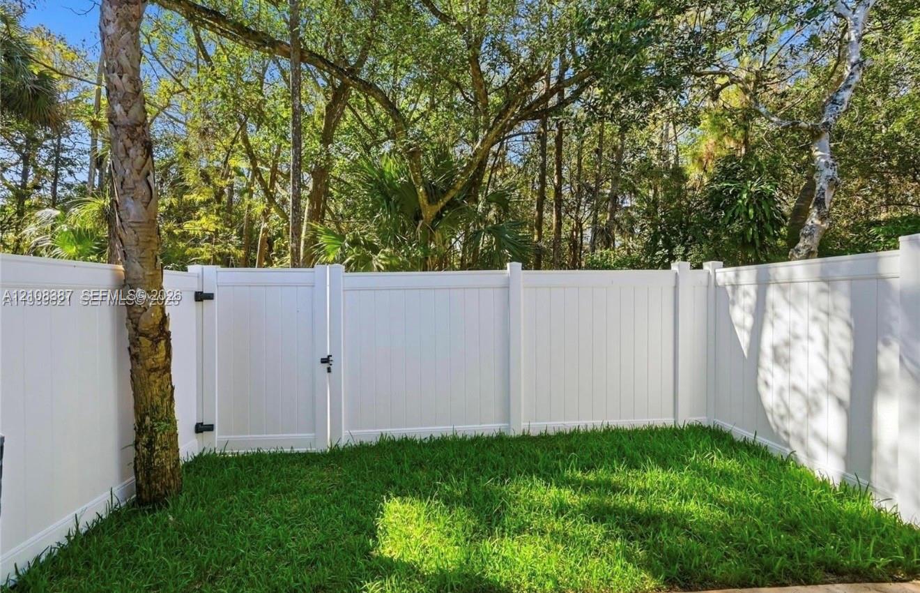 Fenced yard featuring a white vinyl privacy enclosure, gated access, and mature trees
