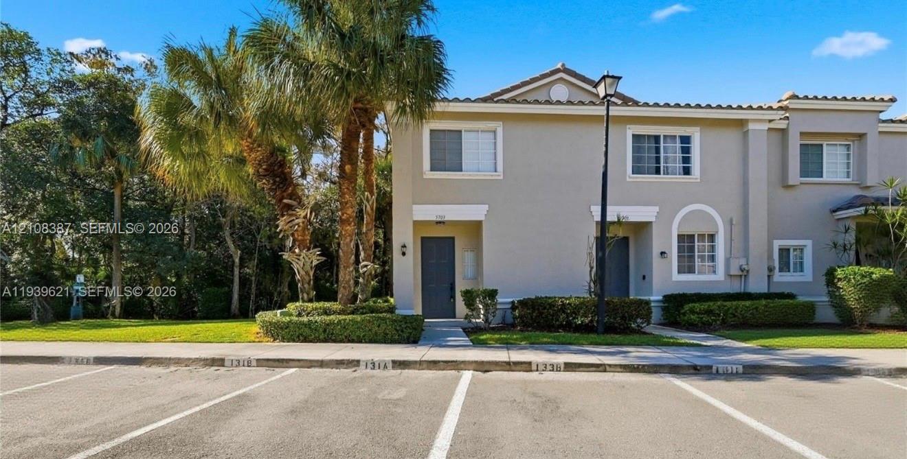 Two-story exterior featuring a neutral stucco facade, tile roofing, decorative arched window detailing, and integrated landscape hedging