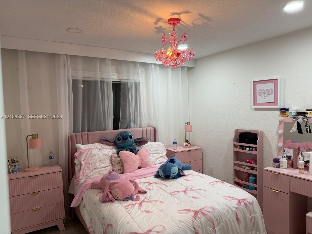 Interior room featuring recessed ceiling lighting, a decorative crystal-style chandelier, and a horizontal window fitted with full-length translucent drapery