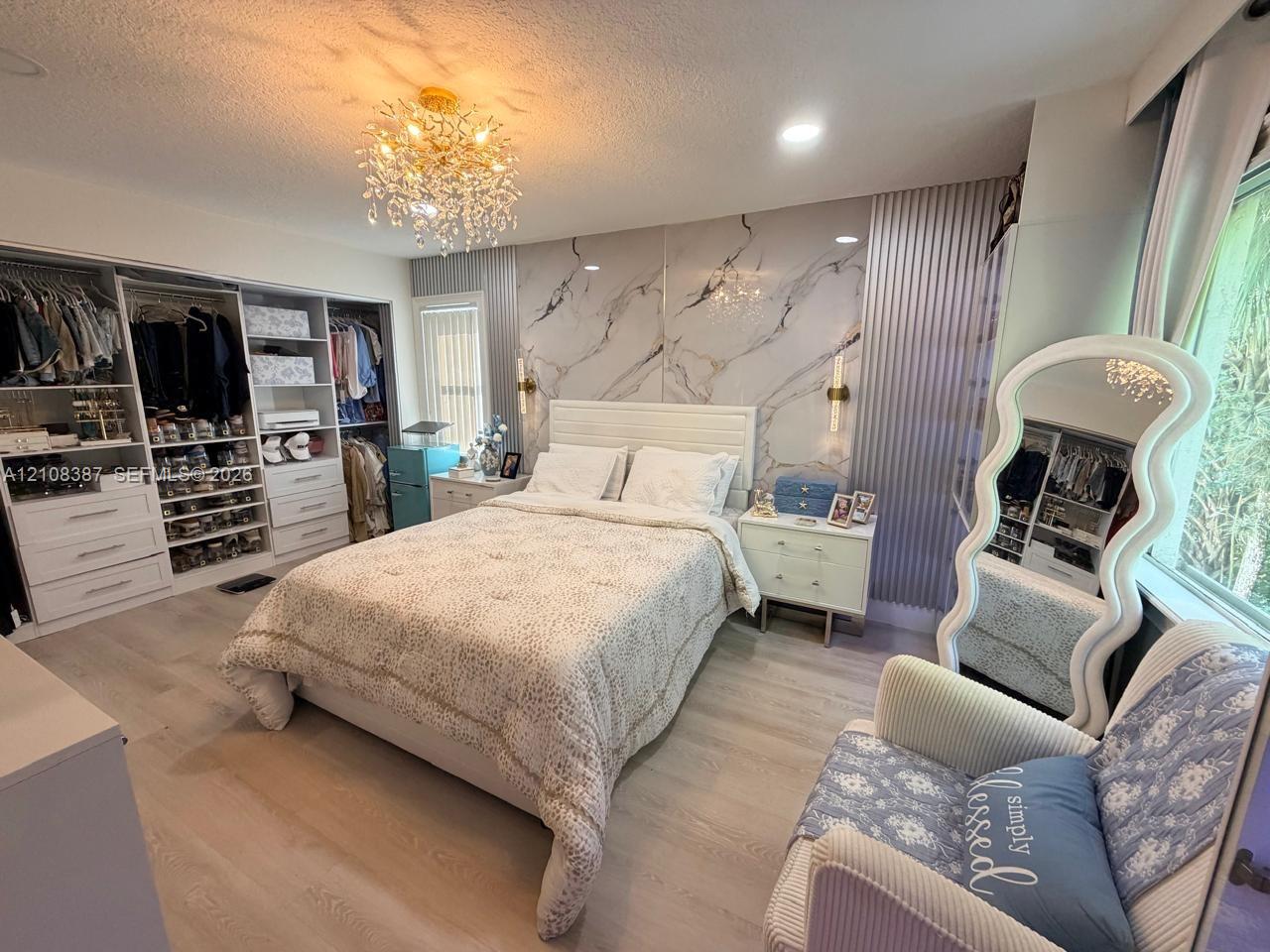 Bedroom featuring wood-finish flooring, a stone-patterned accent wall, a multi-tiered crystal chandelier, recessed lighting, and built-in closet cabinetry
