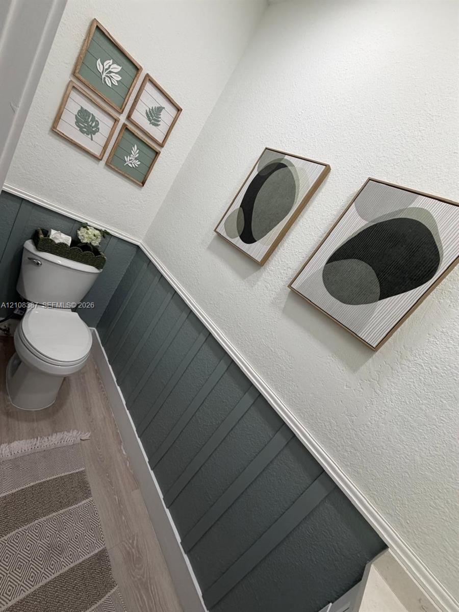 Interior space featuring vertical board-and-batten wainscoting with chair rail molding, light wood-finish flooring, and a standard-height porcelain toilet