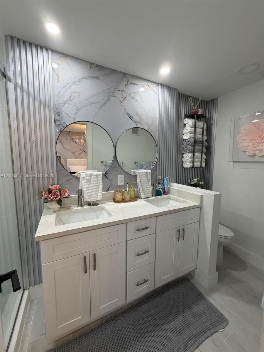 Double vanity featuring white cabinetry, quartz countertop with dual undermount sinks, patterned stone-look accent wall, and circular vanity mirrors