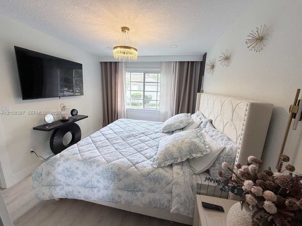 Bedroom featuring wood-finish flooring, a tiered crystal-detail pendant light fixture, and a window with a grid-pattern pane