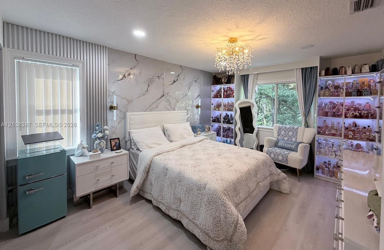 Stone-finish wall accent, built-in floor-to-ceiling shelving with integrated LED illumination, recessed ceiling lighting, crystal chandelier, and wood-finish flooring