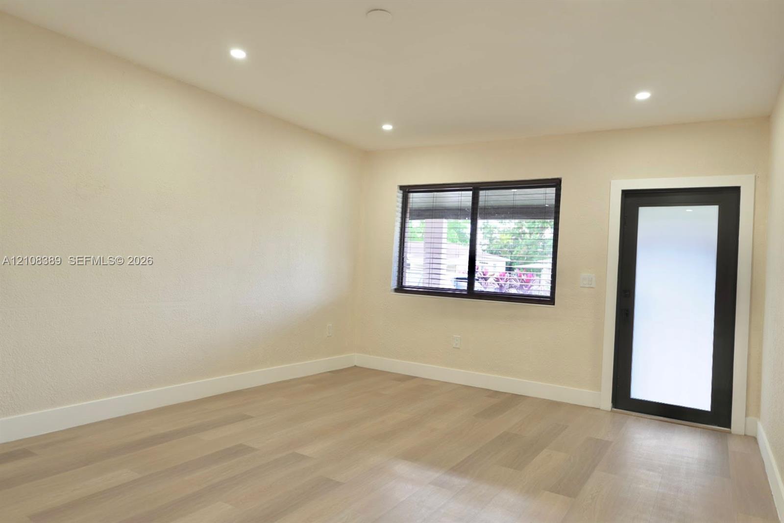 Interior space featuring wood-finish flooring, recessed lighting, textured walls, a single-pane window with dark trim, and a glass-paneled exterior door