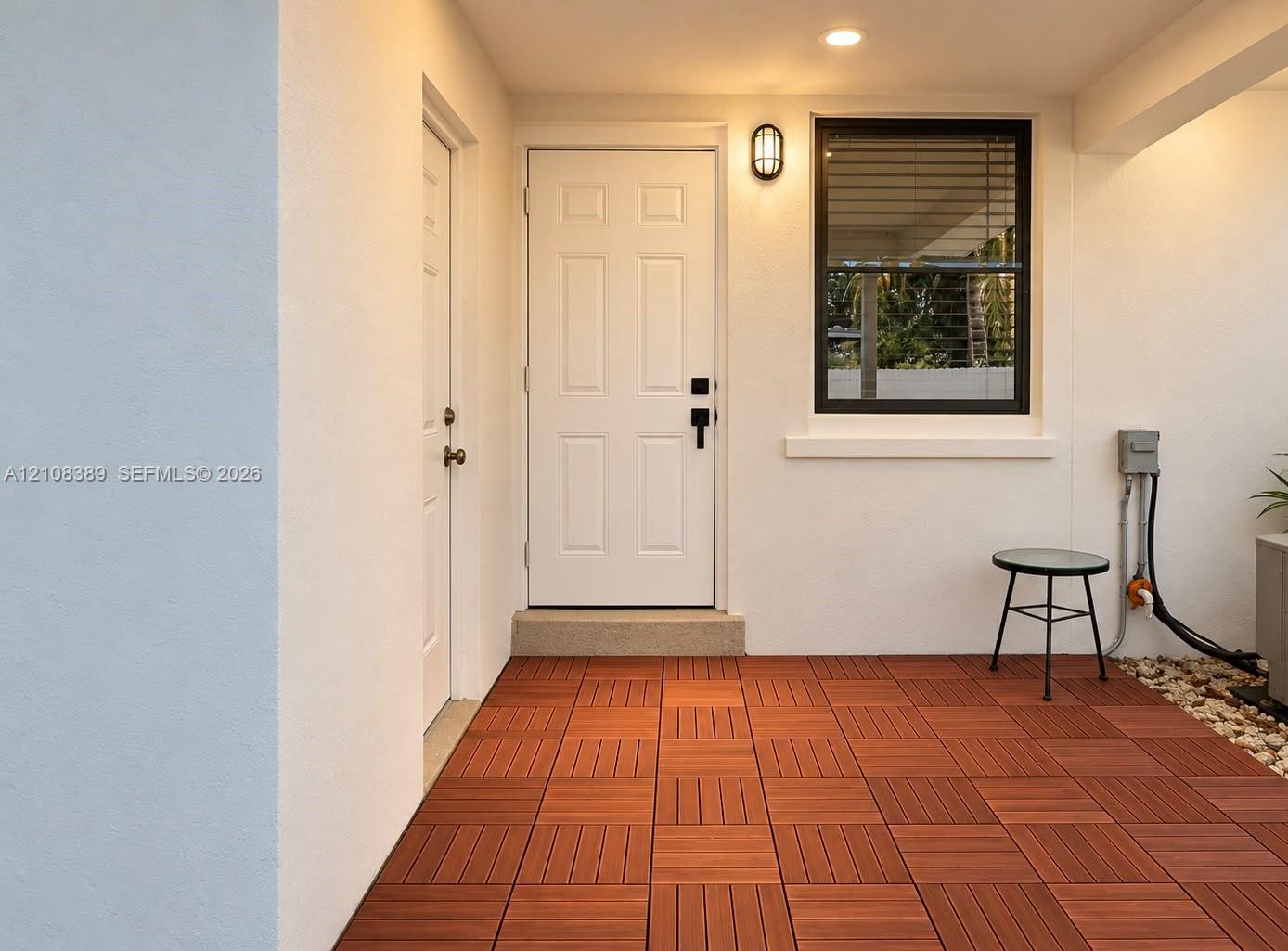 Covered patio featuring wood-finish decking, recessed ceiling lighting, a white six-panel entry door, and a black-framed window