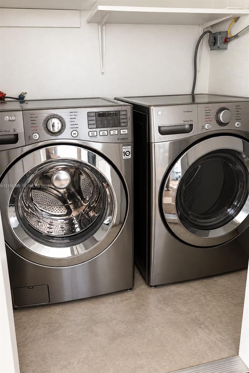 Laundry area featuring stainless steel front-load washer and dryer set, installed wall-mounted metal shelving, and neutral flooring