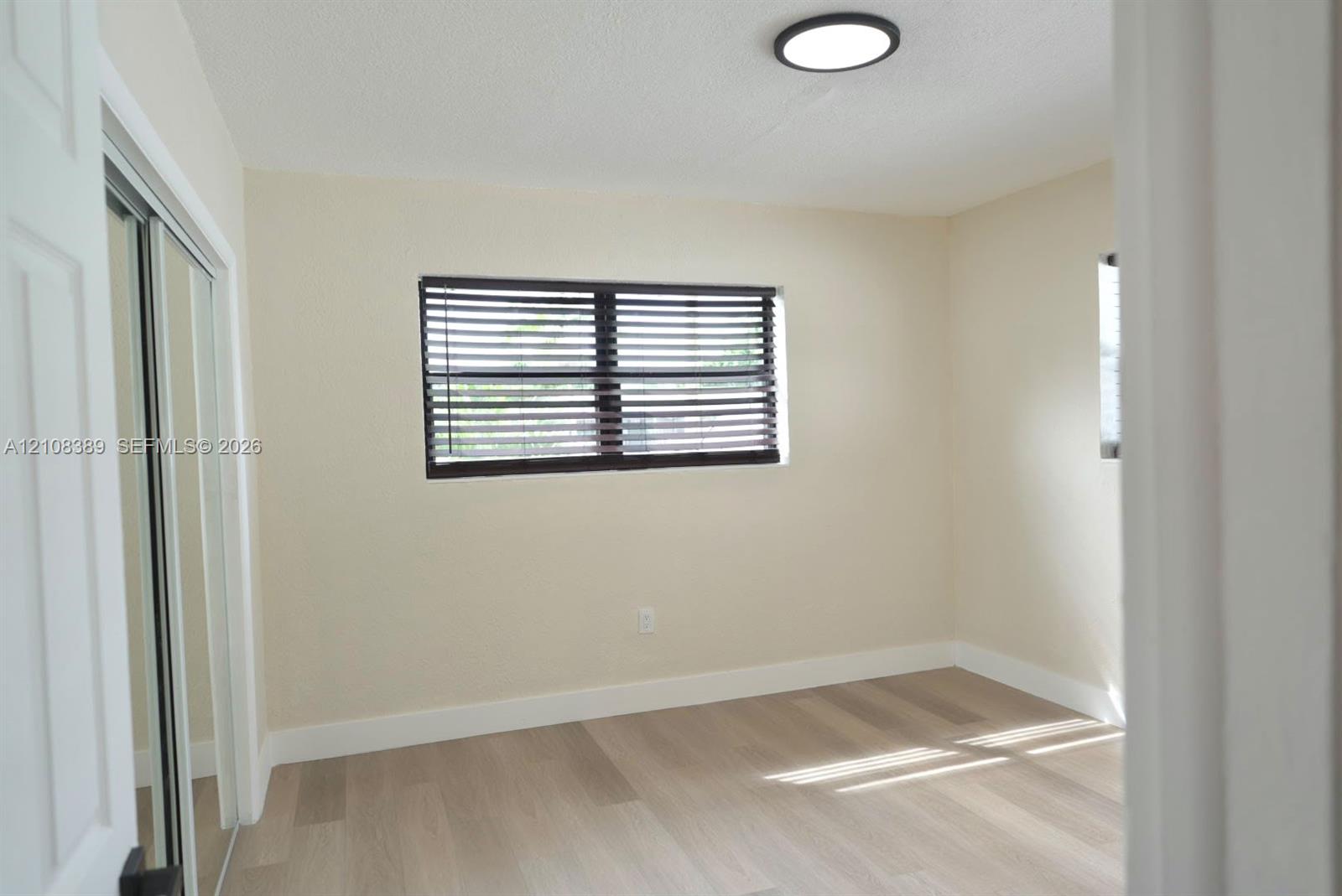 Room interior featuring neutral walls, wood-finish flooring, a sliding mirrored closet, a window with horizontal blinds, and a recessed ceiling light fixture