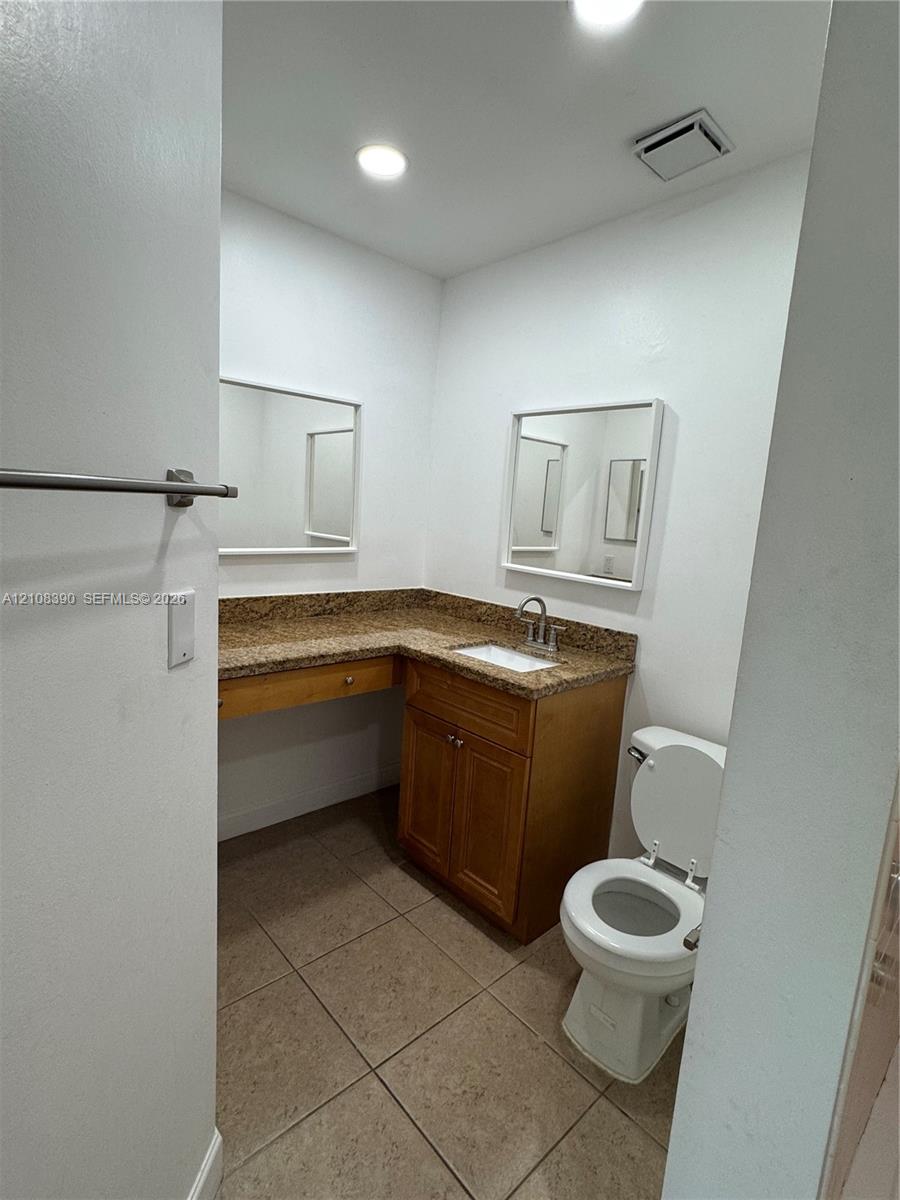 Bathroom featuring wood cabinetry, stone-finish countertop with an integrated basin, recessed lighting, and tile flooring Bathroom featuring wood cabinetry, stone-finish countertop with an integrated basin, recessed lighting, and tile flooring