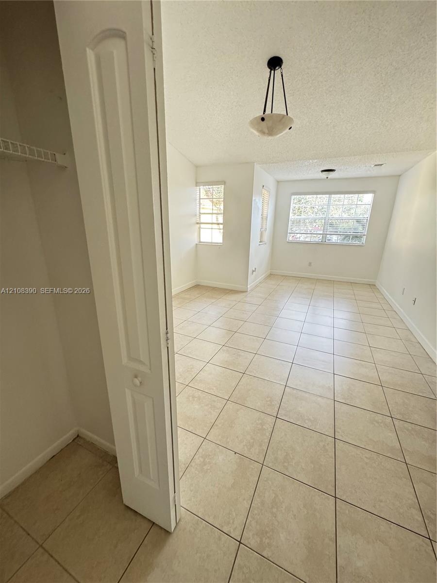 Interior space featuring large-format ceramic tile flooring, neutral walls, multi-pane windows, a built-in closet with bifold doors, and an overhead pendant light fixture