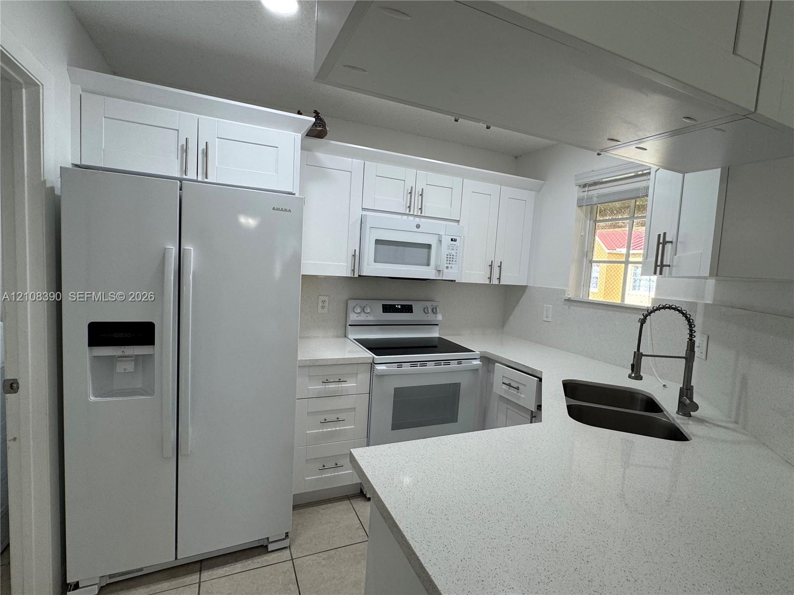 Kitchen featuring white Shaker-style cabinetry, quartz countertops, a dual-basin undermount sink with a gooseneck faucet, a built-in microwave, and tile flooring Kitchen featuring white Shaker-style cabinetry, quartz countertops, a dual-basin undermount sink with a gooseneck faucet, a built-in microwave, and tile flooring