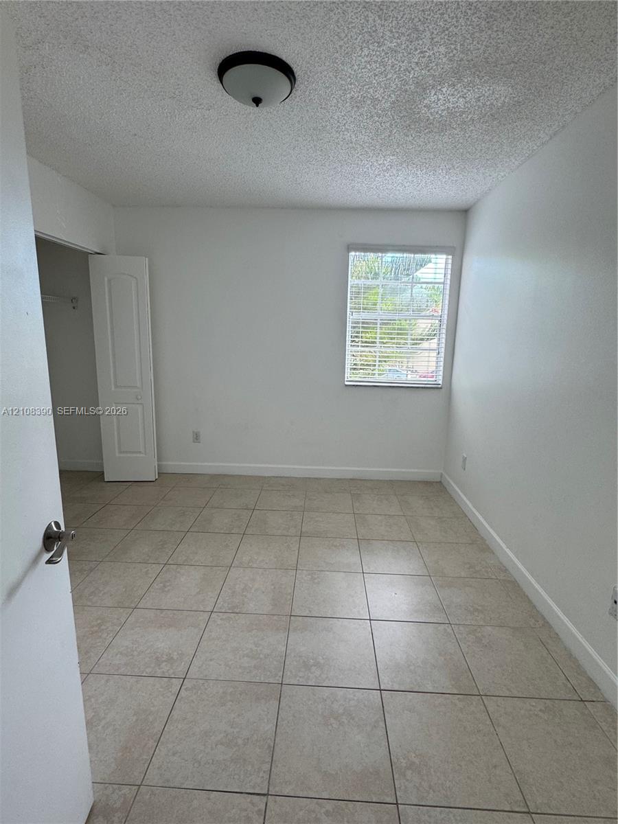 Room featuring neutral-tone tile flooring, a single-panel interior door, a built-in closet, and a window with horizontal blinds Room featuring neutral-tone tile flooring, a single-panel interior door, a built-in closet, and a window with horizontal blinds