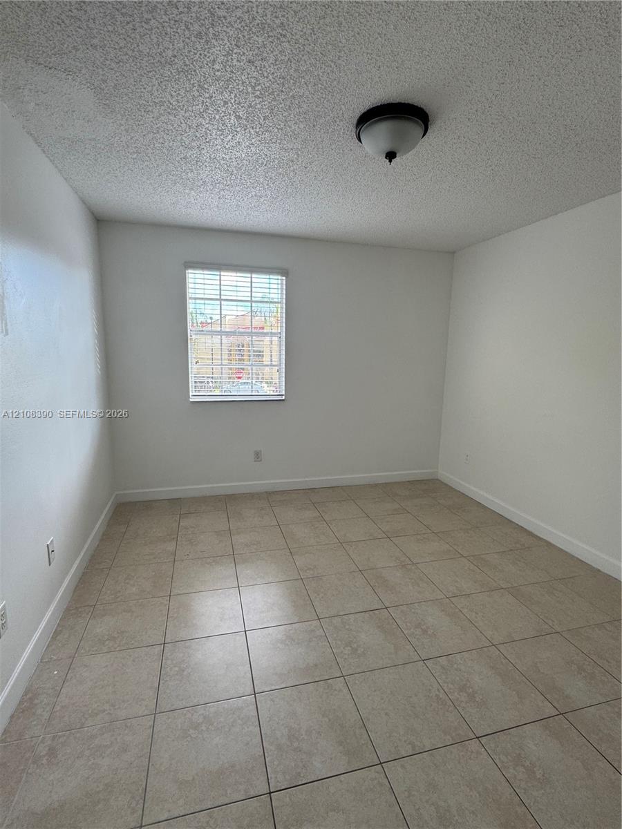 Interior space featuring large-format ceramic tile flooring, neutral wall tones, a single-pane window with internal grids, and a central dome-style ceiling light fixture Interior space featuring large-format ceramic tile flooring, neutral wall tones, a single-pane window with internal grids, and a central dome-style ceiling light fixture