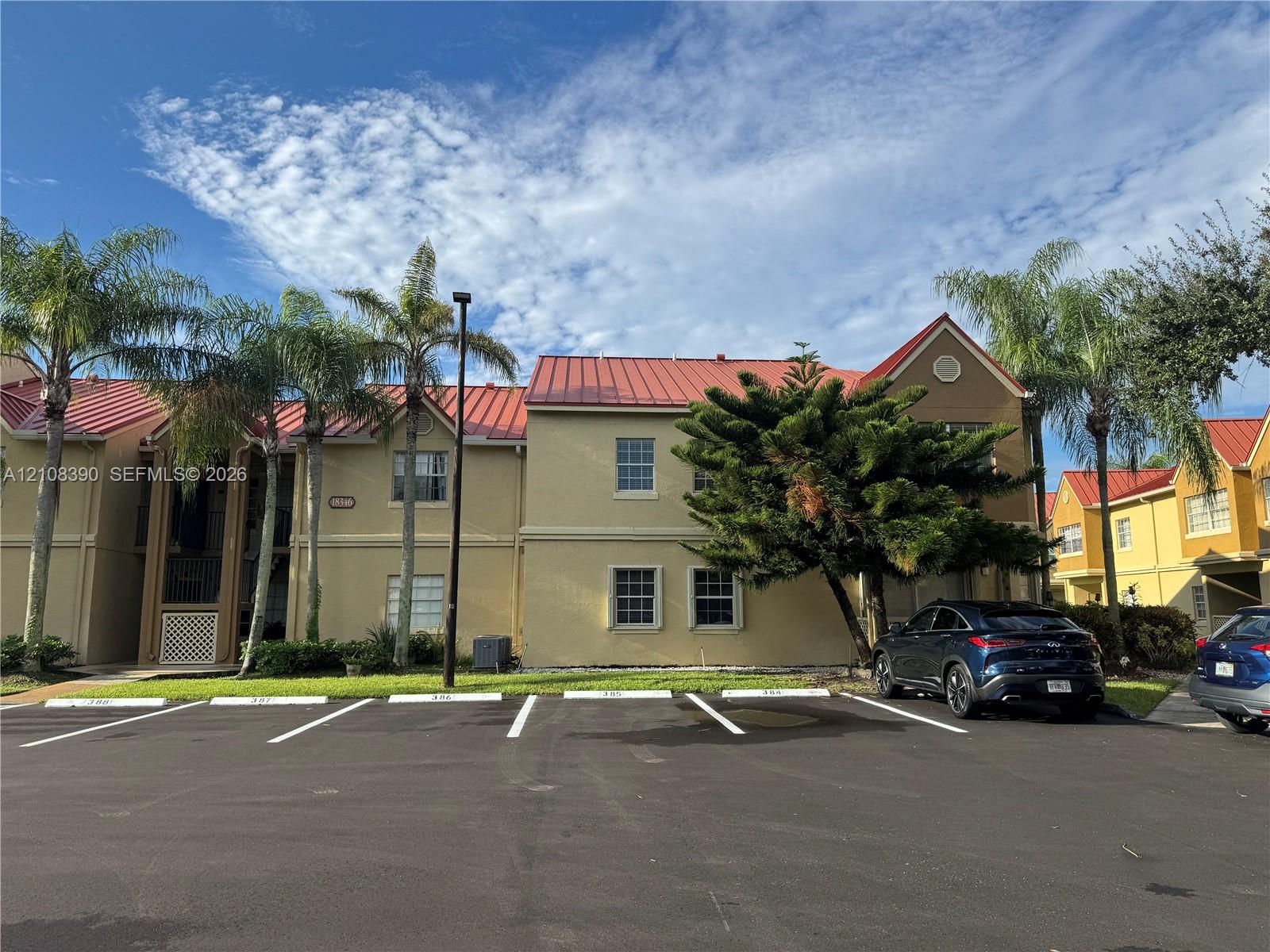 Multi-story stucco exterior featuring a red metal roof, decorative gable trim, and paved surface parking