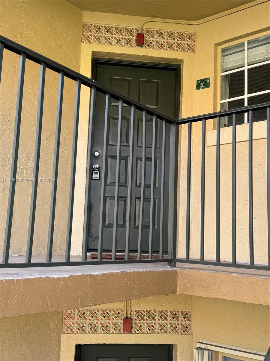 Exterior entry featuring a multi-panel door, metal balcony railing, and decorative tile accents Exterior entry featuring a multi-panel door, metal balcony railing, and decorative tile accents