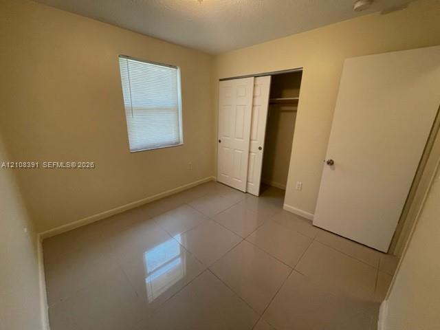 Neutral-toned ceramic tile flooring, sliding bifold closet doors, and a window with integrated blinds