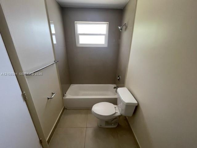 Full-sized bathtub with surround, large-format tile flooring, window, and chrome-finish hardware