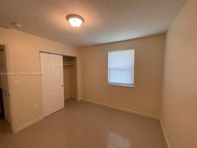 Neutral-toned interior space featuring light-colored tile flooring, a single window with blinds, and a built-in closet with panel doors